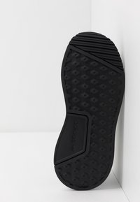 Svart sneaker sula med hexagonalt mönster, texturerade greppsektioner och Adidas-logotyp; platt form med upphöjda accenter vid hälen.