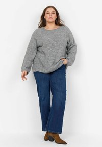 Maglione grigio a maglia con scollatura rotonda e maniche lunghe, abbinato a jeans flared in denim blu e stivaletti marroni con tacco.
