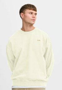 Light green sweatshirt with a rounded neckline, dropped shoulders, and ribbed cuffs. Features a small beige logo on the chest.