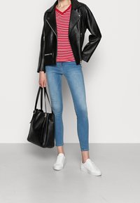Schwarze Lederbikerjacke, rot-weiß gestreiftes V-Ausschnitt-T-Shirt, hellblaue enge Jeans, weiße Sneakers und eine schwarze Handtasche.