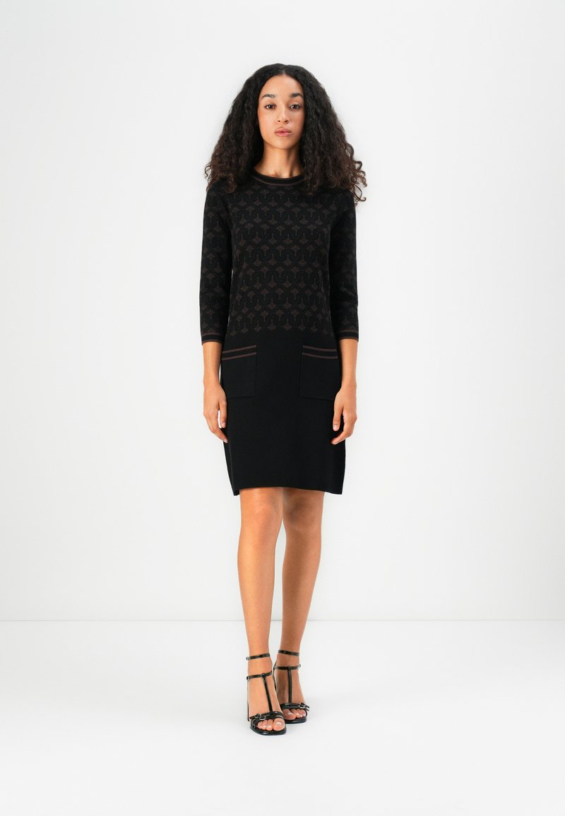 Robe noire avec un haut à motifs et une jupe noire unie. Présente des manches trois-quarts, deux poches avant et une coupe ajustée. Accentuée par des rayures brunes.