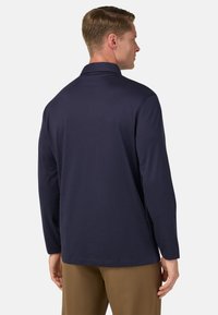 Polo a maniche lunghe di colore blu navy con colletto piatto, texture morbida e orlo dritto. Presenta cuciture minime e una vestibilità rilassata.
