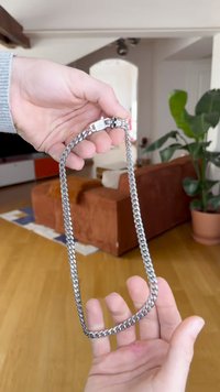 Strieborný kovový náhrdelník s masívnym dizajnom a zapínaním so zdobeným detailom lebky. Hladká textúra a lesklý povrch.