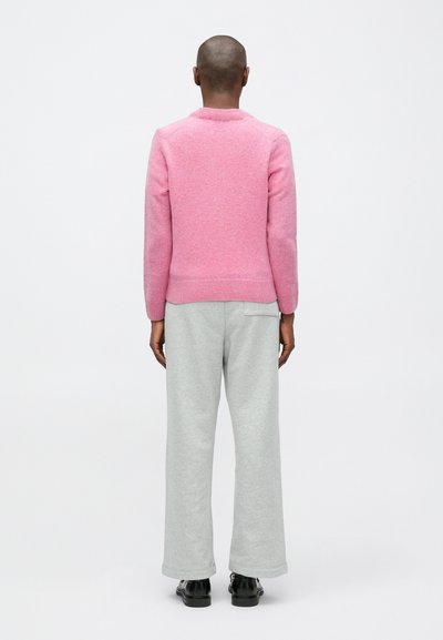 Pulover tricotat roz cu tiv ondulat, asortat cu pantaloni de trening largi gri deschis. Textură netedă și croială lejeră.