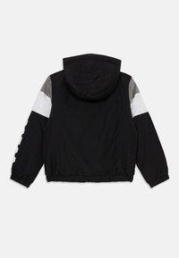 Veste à capuche noire vue de dos, avec des manches en blocs de couleur grise et blanche et des poignets élastiques à l'ourlet.