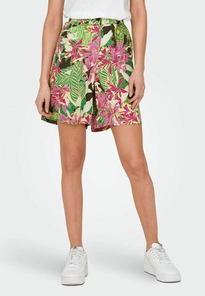 Femme portant un short taille haute à imprimé floral rose et vert, associé à des baskets blanches et un haut blanc.