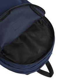 Marinblå tygryggsäck med insida av slät svart foder; dragkedjestängning och en enkel ficka för organisering.