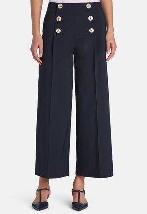 Pantaloni navy a gamba larga con vita alta e doppia fila di sei bottoni beige, indossati con tacchi appuntiti navy con cinturino a T.