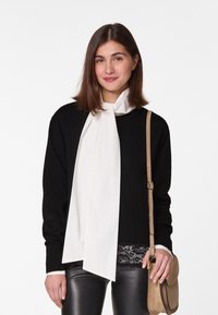 Zwarte trui met lange witte sjaal, gecombineerd met een zwarte kanten top en leren broek. Afgemaakt met een tan crossbody tas en minimale hardware.