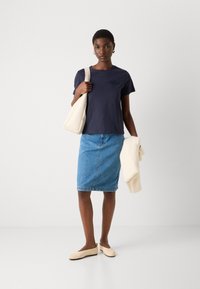 Námornícky bavlnený tričko s logom, modrá denimová ceruzková sukňa, béžové baleríny a krémová kabelka. Hladké textúry a voľný dizajn.