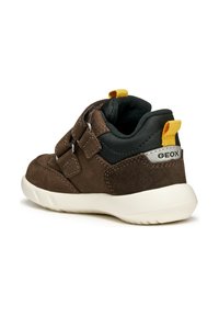 Chaussure en suede marron avec une tige en tissu noir, deux sangles réglables et une languette jaune. Semelle en caoutchouc blanc avec une texture antidérapante.