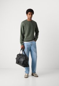 Olivengrøn sweatshirt, lyseblå jeans, sort lædertaske med dobbelte håndtag og cremefarvede sneakers med grønne og brune detaljer.