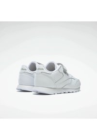 Zapatillas de piel blancas con un acabado suave y acentos en gris claro. Cuenta con una correa de velcro y una suela de goma texturizada.