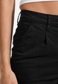 Crna pamukova suknja uskog kroja s bokovima, koja ima bočne džepove i glatku teksturu. Pojas ima suptilan elastik detalj.