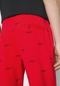 Rote Hose aus glattem Stoff mit schwarzen, gestickten Logos überall. Mit einer Gesäßtasche mit Patch. Schlanke Passform.