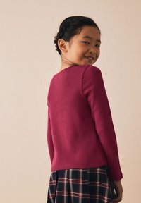 Getailleerde top met lange mouwen in geribbelde fuchsiakleurige stof, gecombineerd met een geruite rok met afwisselend donkere en lichte vierkanten.