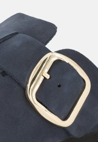 Sandalo in suede blu navy con una fascia larga e una grande fibbia quadrata dorata, caratterizzata da una finitura testurizzata. Fibbia posizionata sul lato esterno.