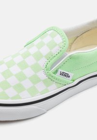 Grønn og hvit rutete slip-on sko i kanvasmateriale, med elastiske sideforsterkninger og en svart gummisåle. Merkevaren er synlig.