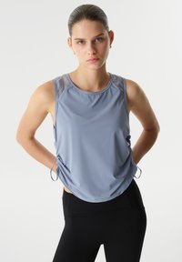 Lichtblauw mouwloos sporttopje met een gladde textuur, voorzien van een ronde halslijn en verstelbare zijstrikjes, gecombineerd met zwarte legging.