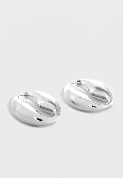 Ζευγάρι γυαλιστερών ασημένιων σκουλαρικιών κρίκων με χοντρό σώμα και λείος, στριφτός σχεδιασμός σε απλό λευκό φόντο.