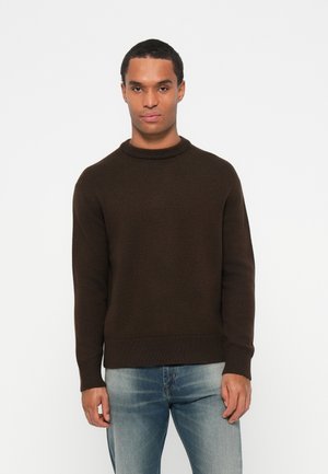 Bruine gebreide sweater met een ronde halslijn en geribbelde manchetten. Draagt over lichtblauwe versleten jeans, met een slim-fit silhouet.