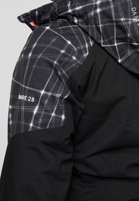 Schwarze Jacke mit einem gesteppte schwarz-weißen Karomuster auf den Schultern. Mit dem "Dare 2B"-Logo in Weiß. Weicher Stoff.