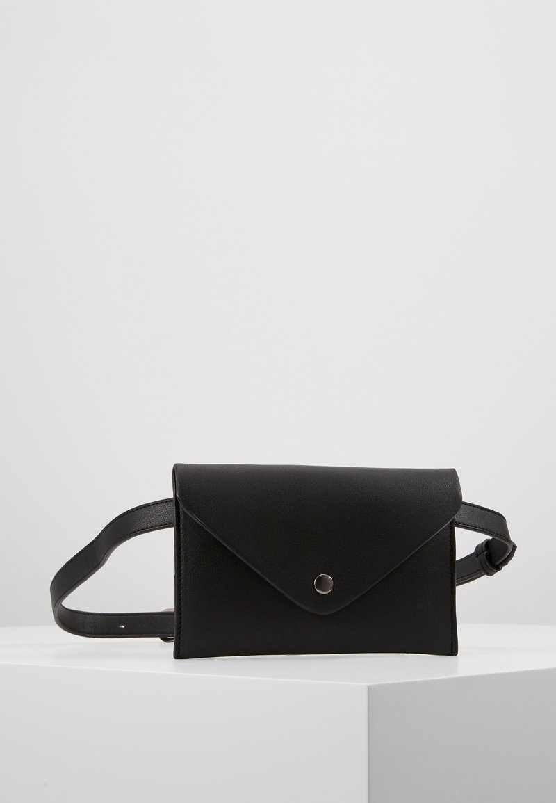 Sac banane en cuir noir avec rabat enveloppe et bouton-pression en métal, présenté sur une surface blanche sur un fond uni.