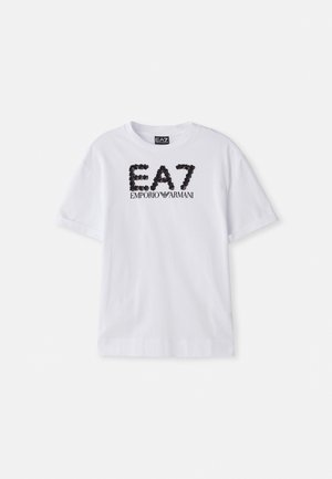 Valkoinen puuvillapaita, jossa on mustat paljeteilla koristeltu logo "EA7 EMPORIO ARMANI" edessä, lyhyet hihat ja pyöreä pääntie.