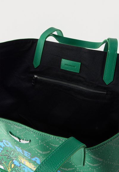 Πράσινη τσάντα tote με μαύρη επένδυση, πράσινα χερούλια, εσωτερική τσέπη με φερμουάρ και πολύχρωμο σχέδιο που φαίνεται μερικώς εξωτερικά.