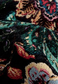 Textil s farebným kvetinovým a listovým vzorom v čiernych, zelených, červených a zlatých textúrach. Tkanina pôsobí ako tkaná a má jemný dotyk.