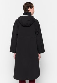 Zwarte waterdichte jas met een aangesloten capuchon, lange mouwen en een knielange snit. Heeft een minimalistische stijl en geen zichtbare hardware.