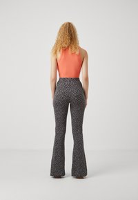 Ribbed orange tank top paired with high-waisted, flared black pants featuring a small leopard print pattern. Back view with textured hair.