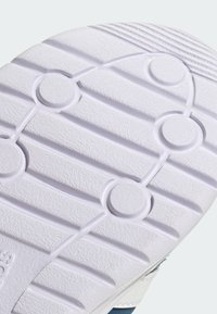 Biela podrážka topánky s textúrovaným povrchom, ktorý obsahuje kruhové a lineárne vzory; súčasť dizajnu športovej tenisky.