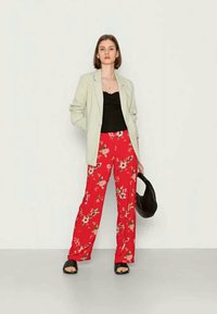 Blazer cinza claro sobre uma blusa regata preta, combinado com calças largas de estampado floral vermelho e sandálias de slide pretas. Uma bolsa preta realça o conjunto.