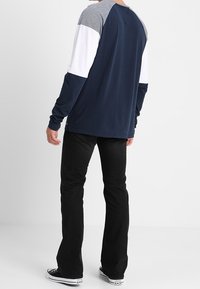 Mörkblå långärmad skjorta med grå och vita raglanärmar. Matchad med svarta utsvängda jeans och svarta sneakers. Slät textur.