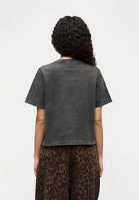 Γκρι μπλουζάκι με κοντά μανίκια, άνετη εφαρμογή, στρογγυλή λαιμόκοψη και διακριτική ξεθωριασμένη υφή, σε συνδυασμό με καφέ φούστα με λεοπάρ σχέδιο.