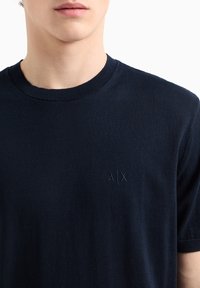 T-shirt en coton bleu marine avec col ras du cou, arborant un subtil logo brodé "A|X" sur la poitrine, texture lisse et manches courtes.