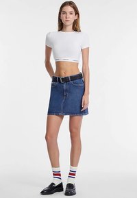 Chemise blanche courte, jupe en jean bleu avec une ceinture noire, et mocassins noirs. Les chaussettes présentent des rayures rouges et bleues. Look propre et décontracté.