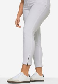 Pantalones vaqueros blancos con un diseño ajustado, que cuentan con cremalleras laterales en los puños. Combinados con zapatillas blancas con acentos grises.