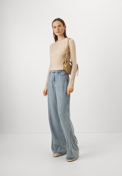 Pull en tricot côtelé beige, jeans bleu clair à jambe large, sac à main beige et chaussures de couleur claire. Textures lisses et coupe décontractée.