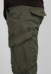Pantalons cargo en coton vert foncé avec plusieurs poches, y compris une poche à rabat. Texture douce, coutures durables et coupe décontractée.