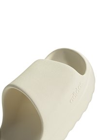 Infradito bianche con una finitura testurizzata, apertura sul retro e una fascia larga, con il logo Adidas in rilievo sul lato.