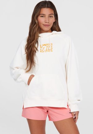 Sweat à capuche crème avec poche avant et imprimé "Women of the Wave" en jaune. Doté d'une capuche, de manches longues et de poignets côtelés. Accompagné de shorts roses.