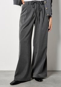 Pantaloni a gamba larga in tessuto grigio a righe, con cintura legata, tasche frontali e una texture liscia, abbinati a scarpe nere.