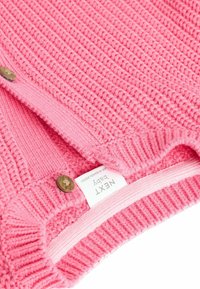 Pull en laine rose pour bébé avec des côtes texturées, muni de deux boutons ronds et d'une étiquette visible sur l'ourlet intérieur. Tissu doux et confortable.