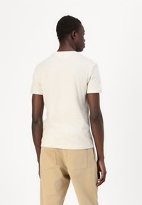 Lys beige kortermet t-skjorte laget av bomull, med en klassisk rund hals og en jevn tekstur, kombinert med brune bukser.