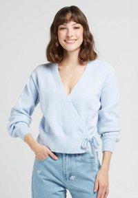 Un pull enveloppant tricoté bleu clair avec un décolleté en V profond, des manches longues, des poignets côtelés et un détail à nouer à la taille. Texture douce.