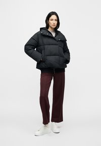 Čierna prešívaná bunda s kapucňou, s prešívaným vzorom, zapínaním na cvoky a rebrovanými manžetami, v kombinácii s bordovými nohavicami a bielymi teniskami.