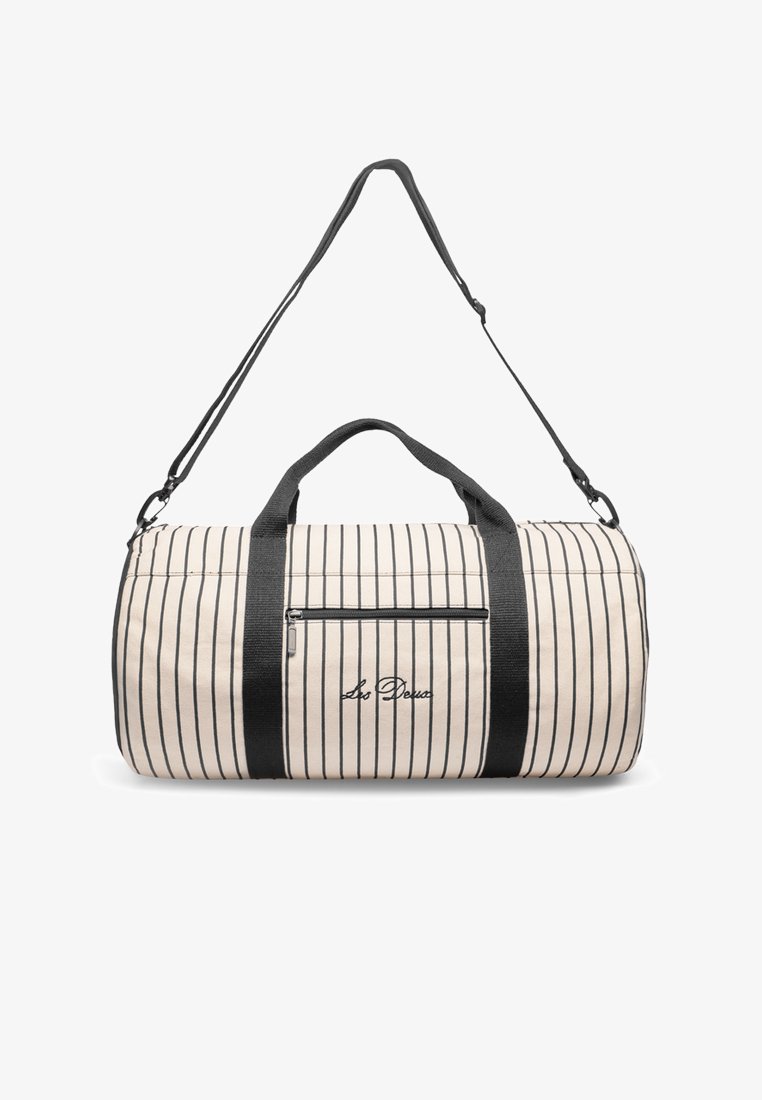 La bolsa de lona presenta un patrón a rayas crema con acentos negros, doble asa y una correa de hombro larga y ajustable. Incluye un bolsillo frontal con cierre.