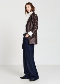 Blazer en cuir marron avec design structuré, associé à un pantalon en denim large bleu marine. Le mannequin porte un top à col blanc en dessous.